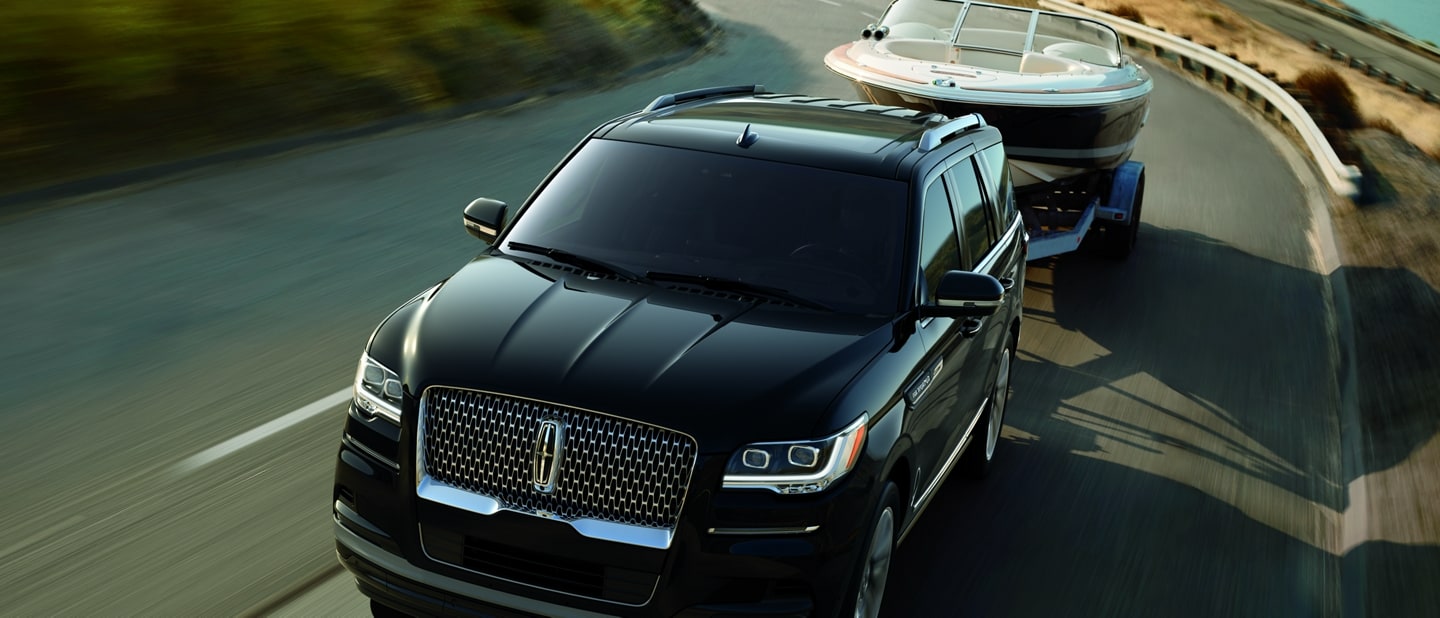 A 2024 Lincoln Navigator® SUV towing a boat is being driven along a curving road