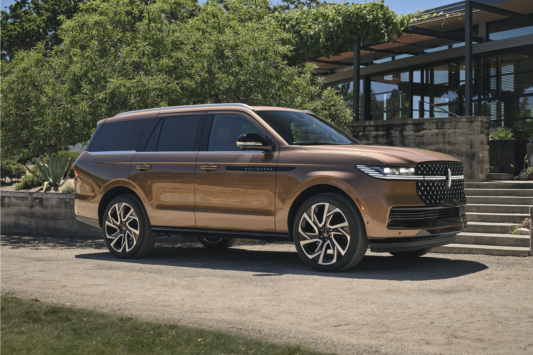 A 2025 Lincoln Black Label Navigator® SUV is parked next to a modern home surrounded by lush greenery.