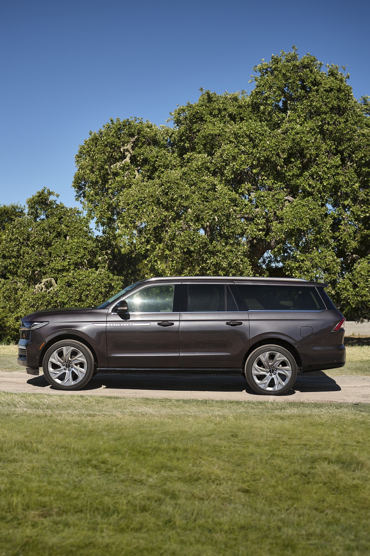 A 2025 Lincoln Navigator® SUV with the long wheelbase is parked in a tree line road