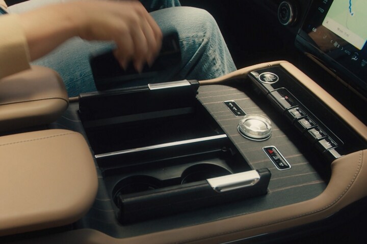 The driver of a 2025 Lincoln Black Label Navigator® SUV reaches to place a smartphone on the wireless charging pad